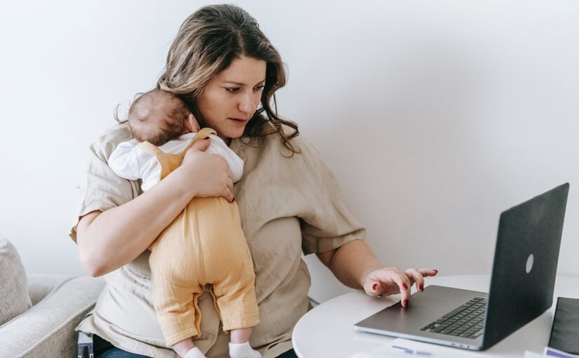 young working mother cuddling baby and using laptop at home
